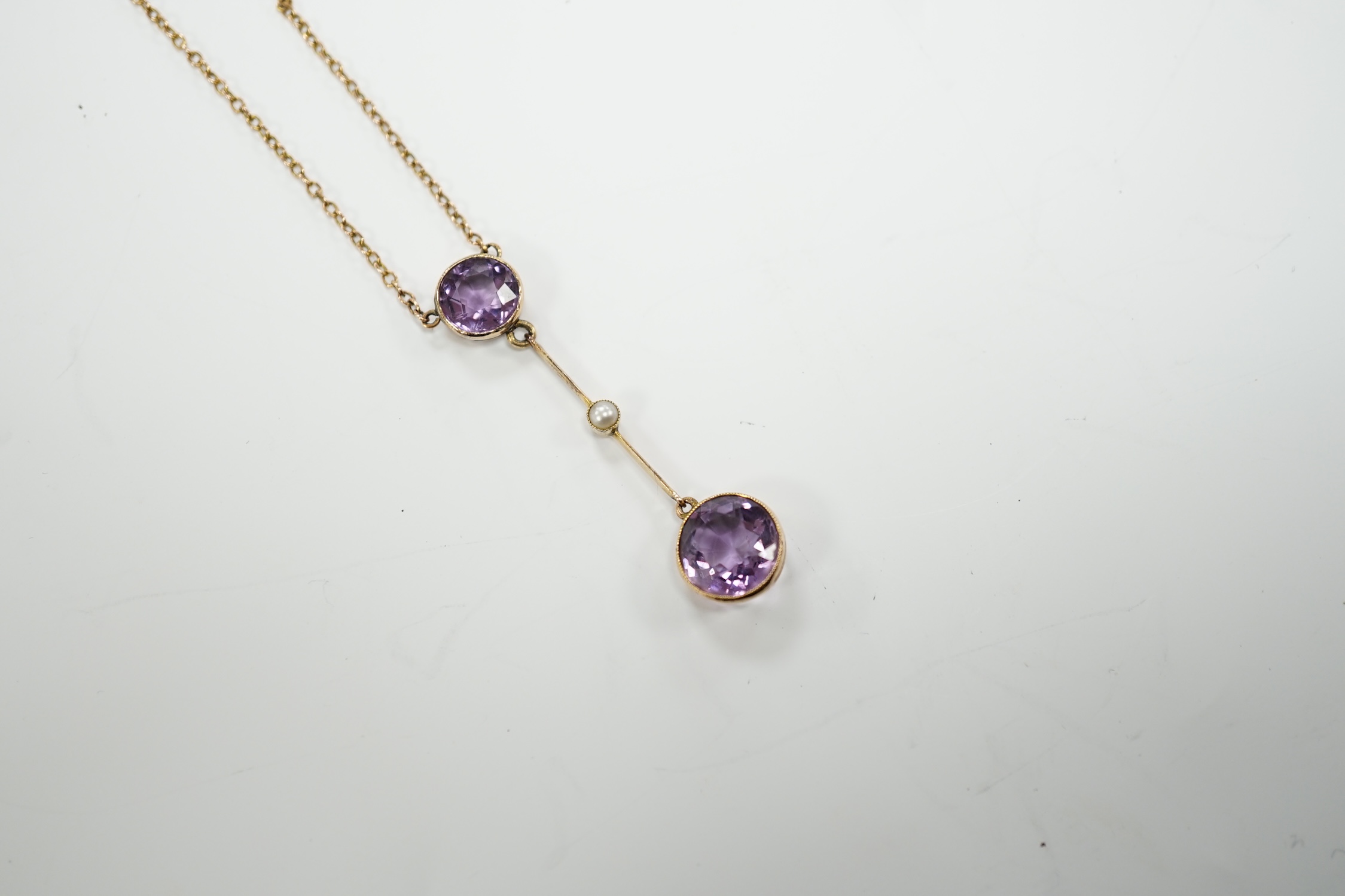 An Edwardian 9ct, two stone amethyst and single stone seed pearl set drop pendant necklace, gross weight 3.8 grams.